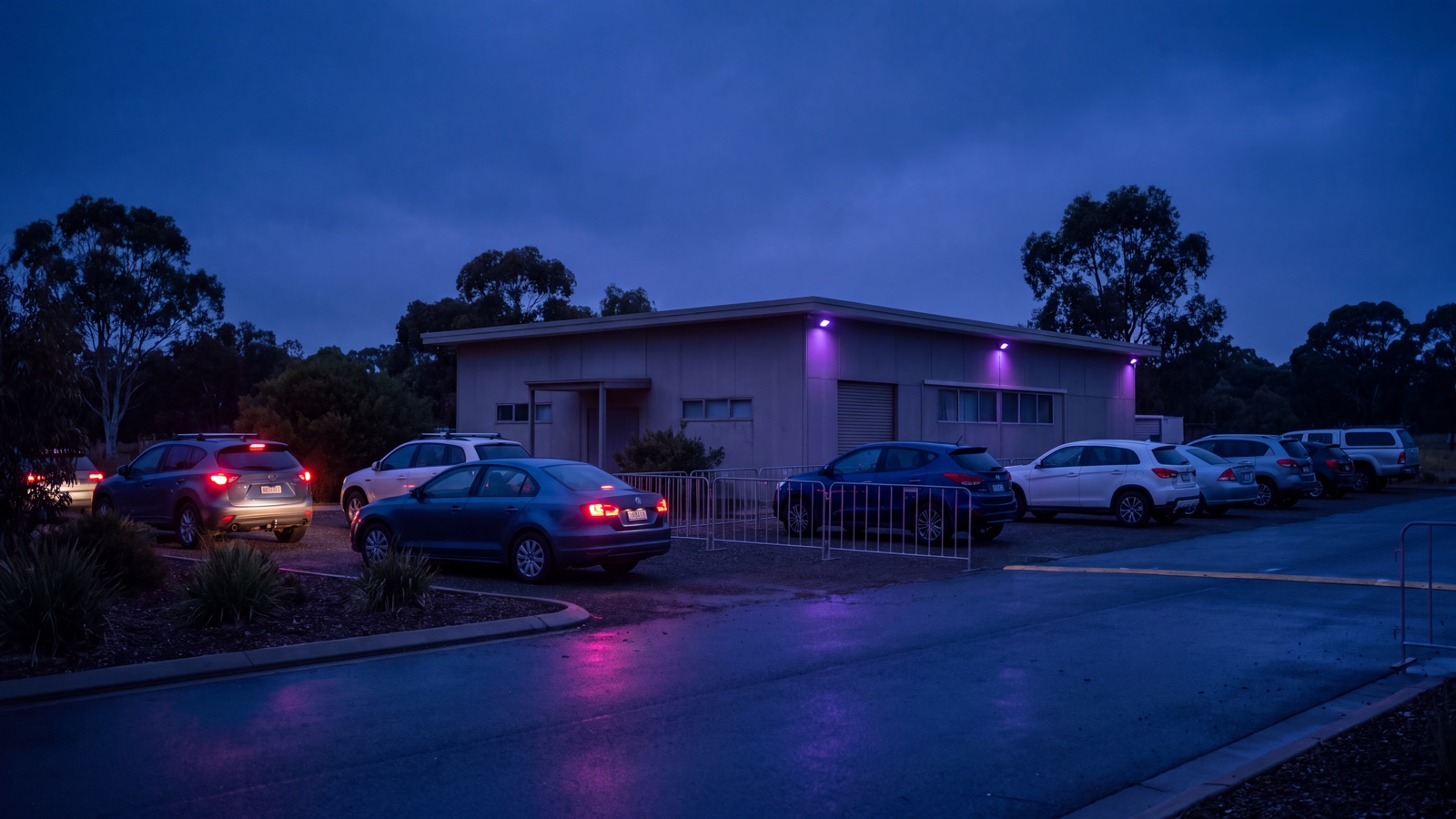 Generic regional event precinct at dusk with ordinary parked vehicles, a plain pavilion and restrained purple practical lighting.