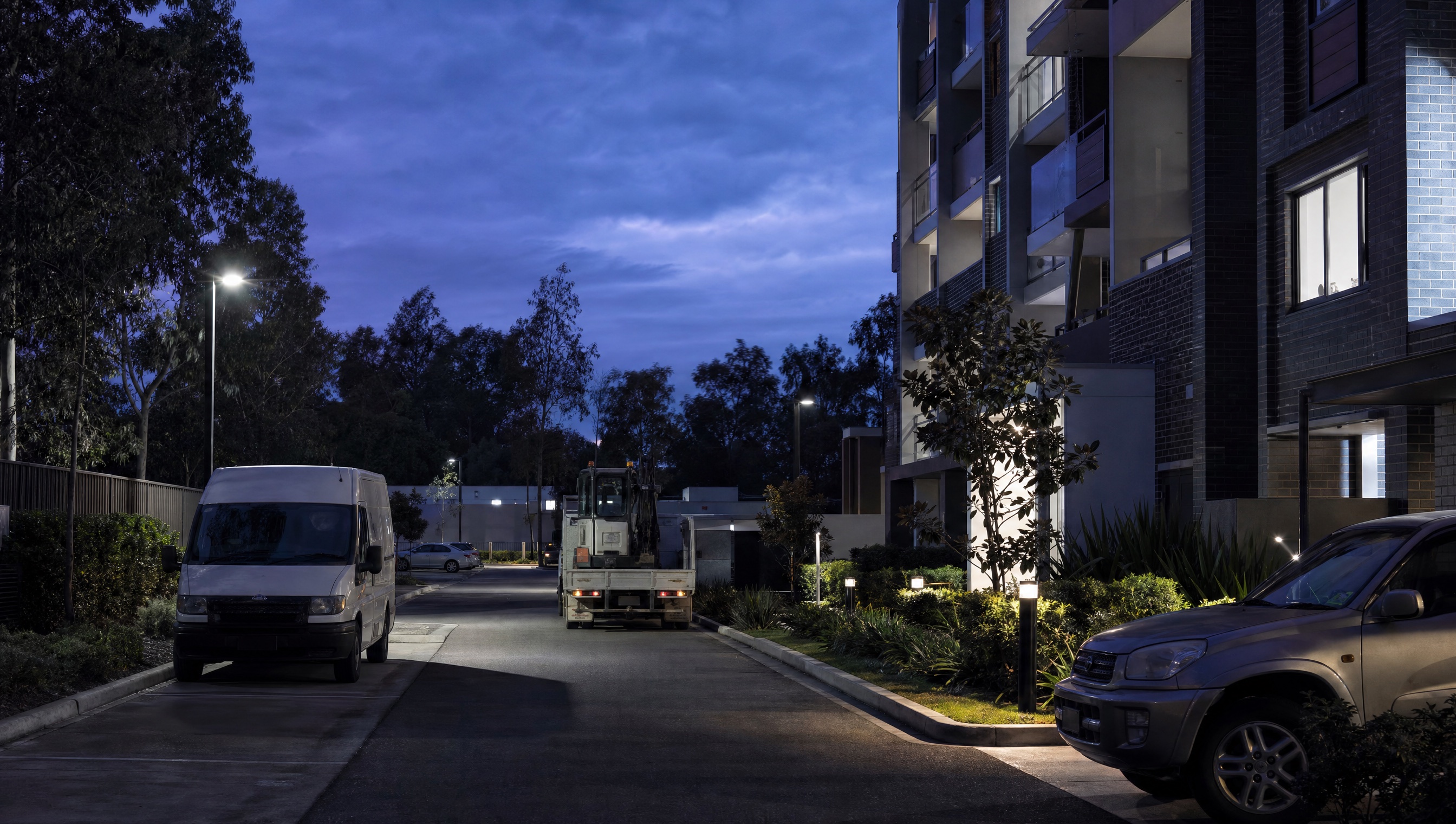 Residential community loading and contractor parking area beside apartment buildings at dusk